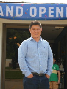 Man smiling under grand opening banner outside building